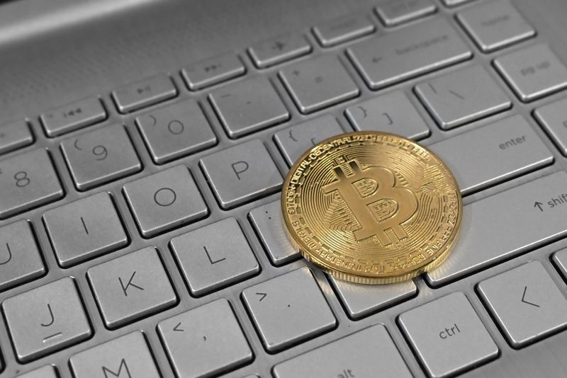 Moneda física dorada con el símbolo de bitcoin sobre el teclado de un portátil