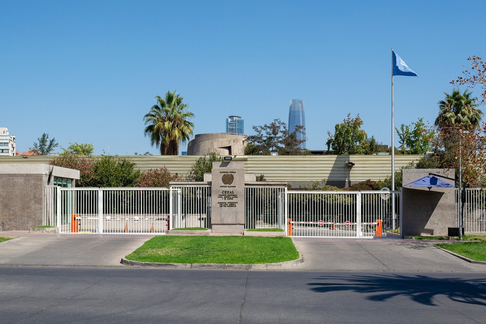 Entrada del edificio de la CEPAL en Vitacura, Santiago de Chile, con jardines, palmeras y una bandera