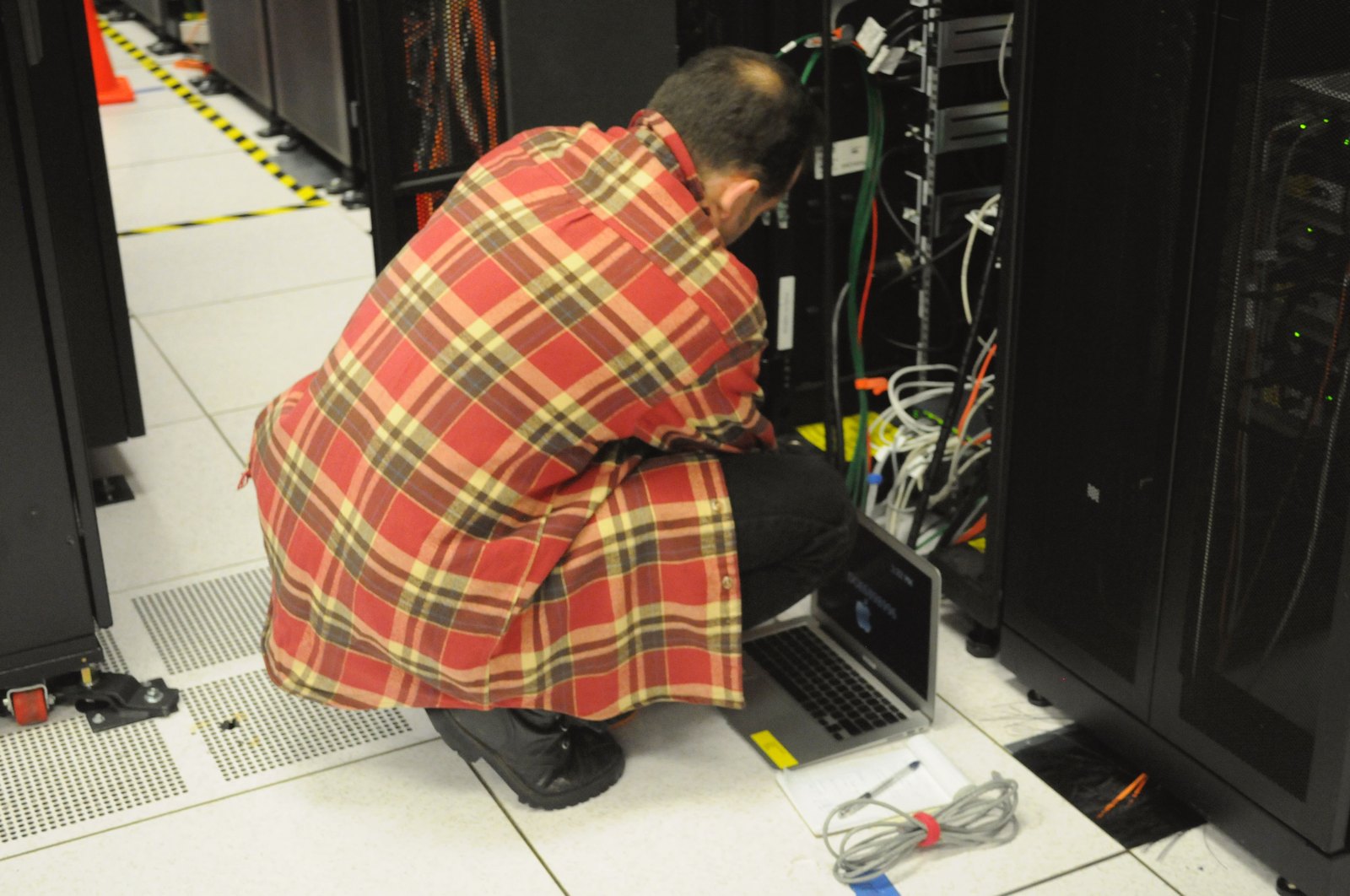 Técnico agachado con una laptop conectada a un rack de servidores en un centro de datos