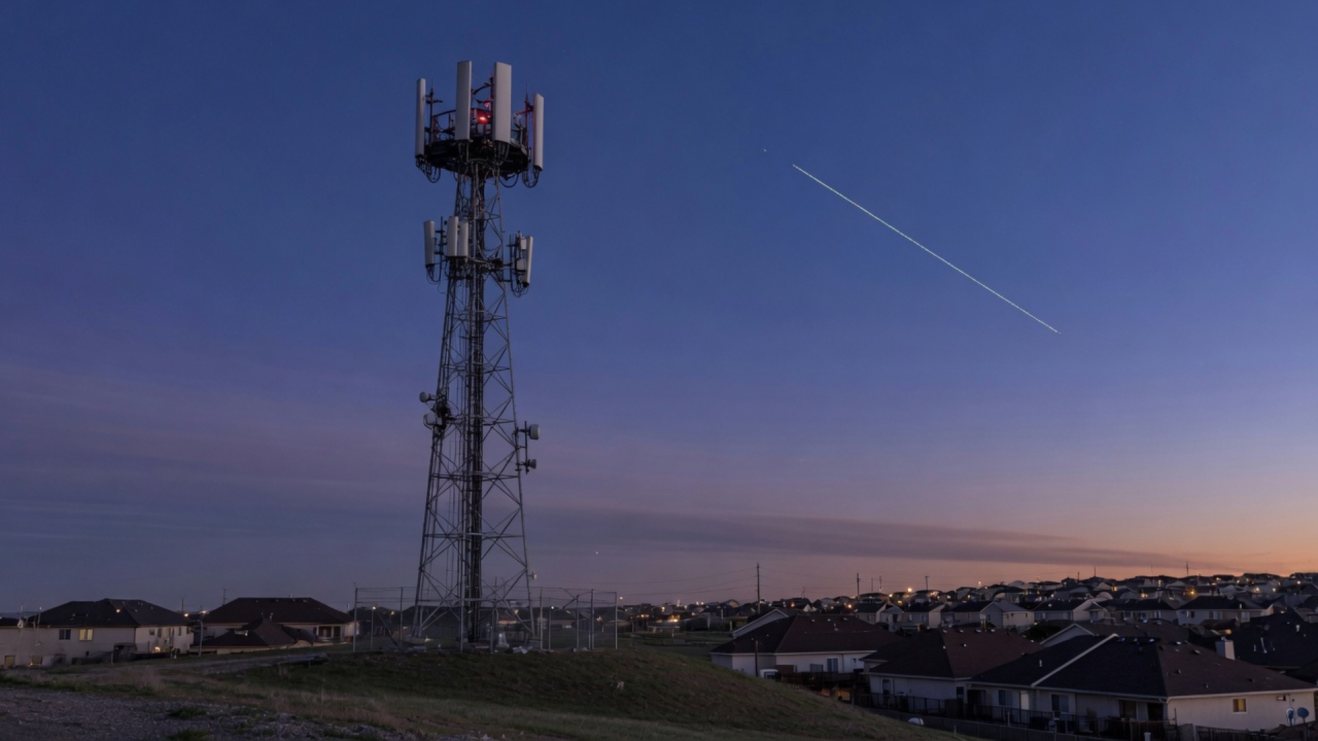 Torre de telefonía móvil al anochecer con un rastro de satélite en el cielo, imagen ilustrativa.